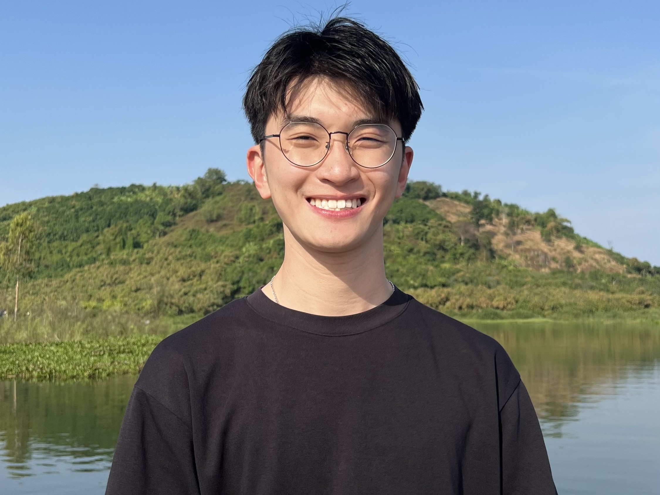 Tran Minh Quan smiling in front of a lake and mountain in Kyoto